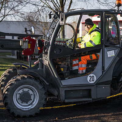 Lächelnder ELSTERWERK-Mitarbeiter in gelber Warnschutzkleidung auf grünem John Deere Geländefahrzeug bei Landschaftspflege-Arbeiten